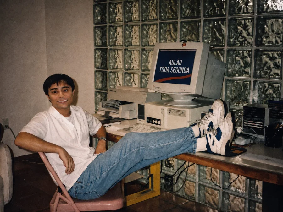 Foto antiga de um estudante em frente ao computador, com um aulão do Aprova Total na tela